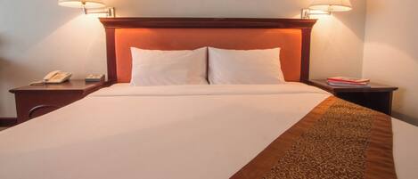 Una habitación de hotel con una cama grande, dos lámparas de noche, un teléfono y una mesita con libros.