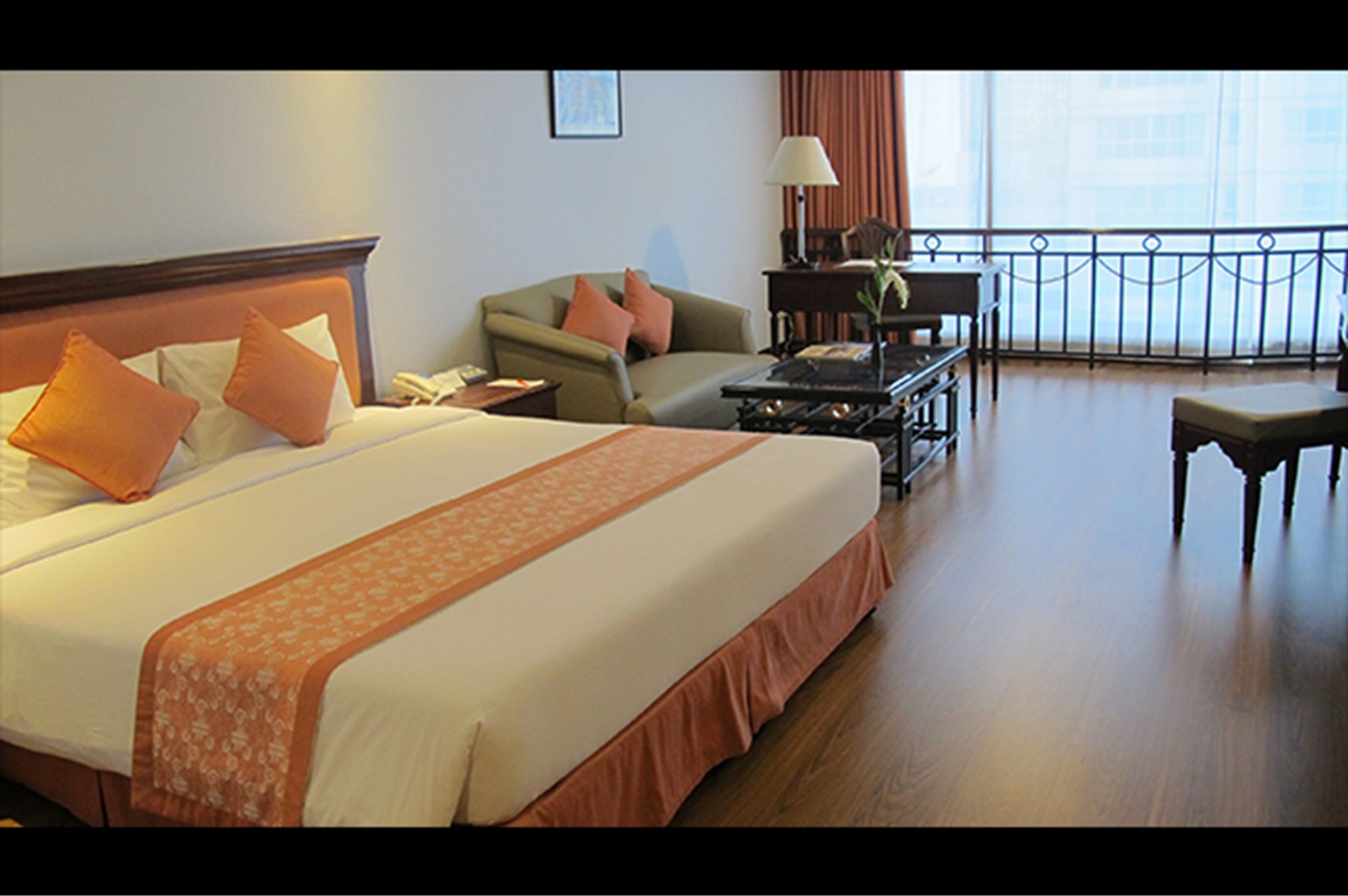 A hotel room with a large bed, a sofa, a desk, and a balcony with a railing.