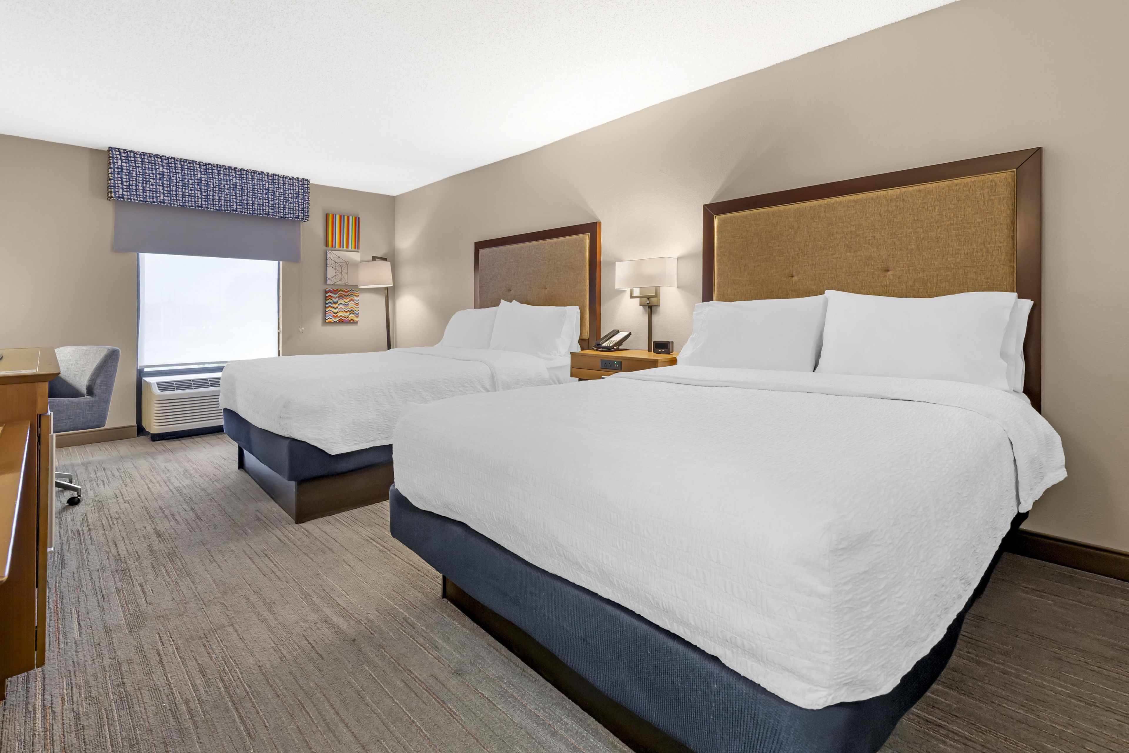 Ein Hotelzimmer mit zwei Betten, einem Schreibtisch, einem Stuhl und einem Fenster mit Jalousien.