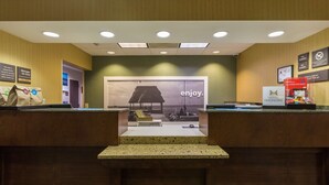 Zona de recepción de un hotel con un cartel grande que dice 'enjoy', un mostrador con una computadora y un letrero que indica un tiempo de registro de 45 minutos.