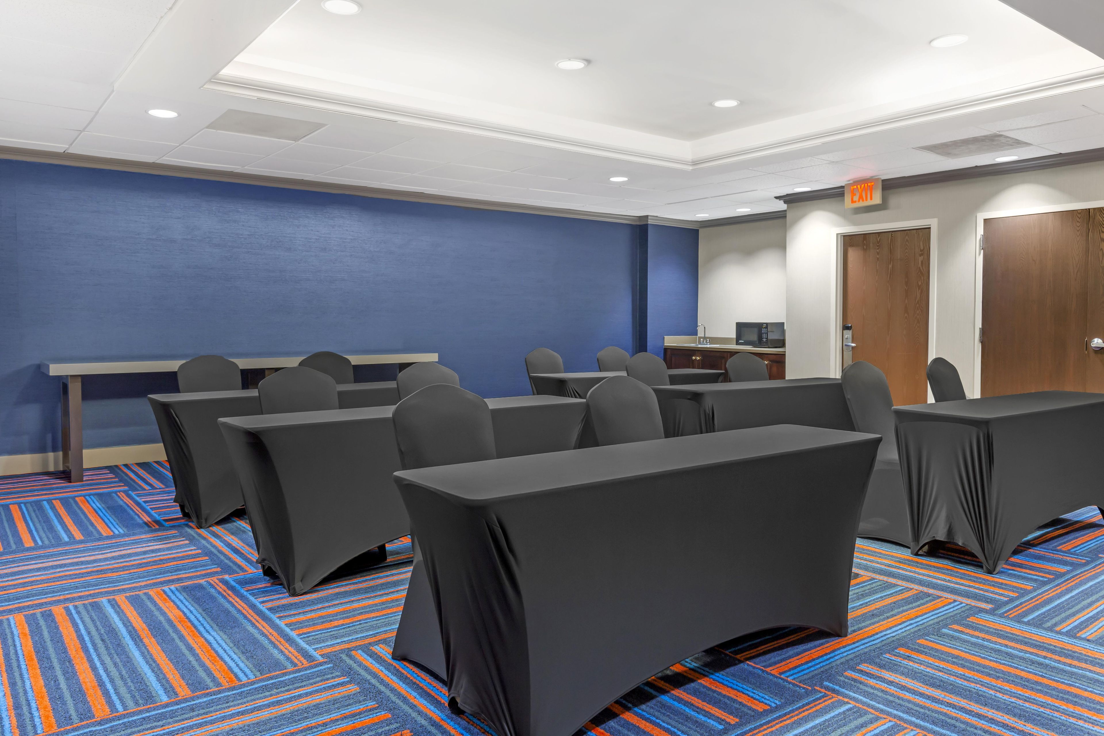 Un salón de conferencias con mesas y sillas, una pared de acento azul y una señal de salida.