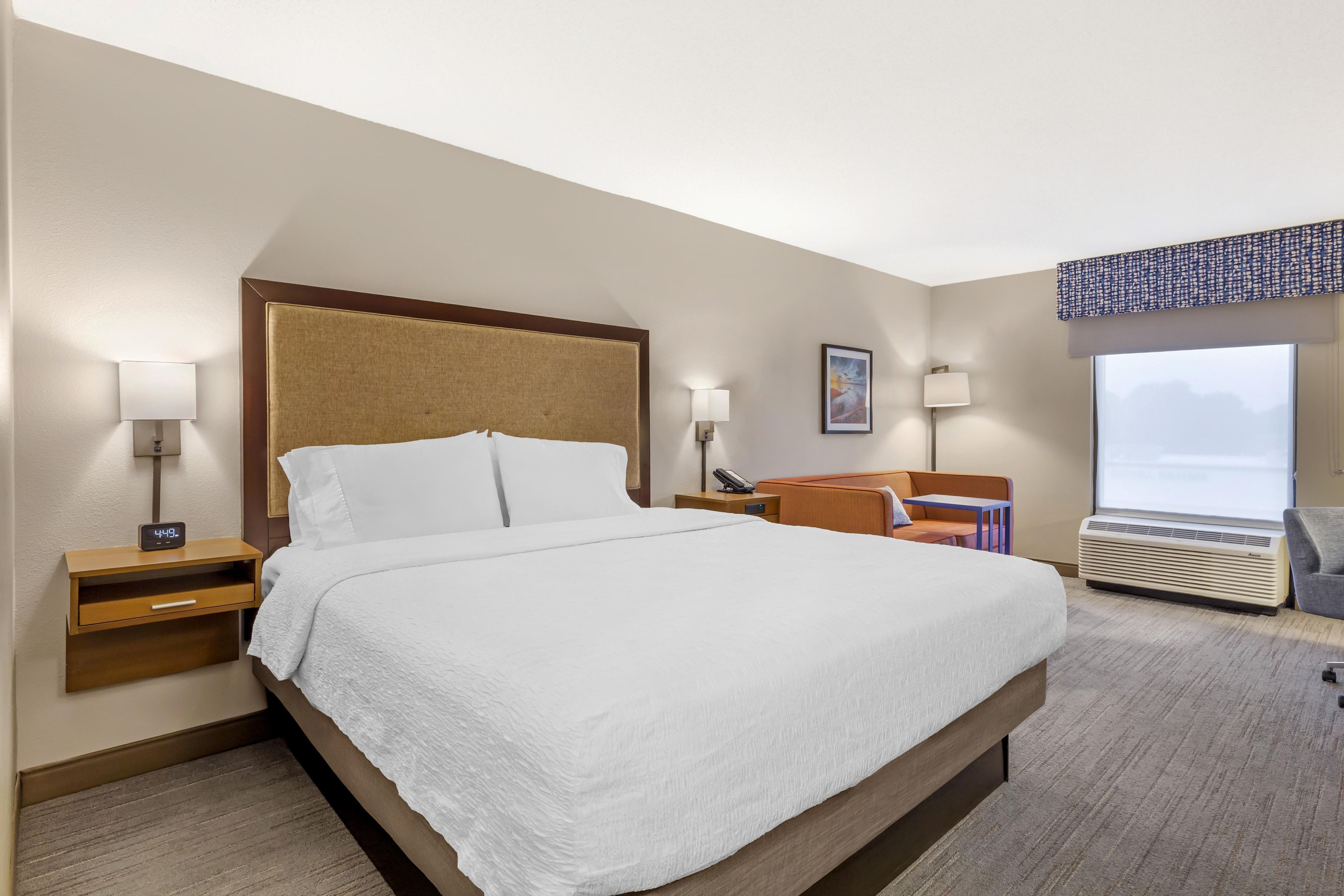 A hotel room with a large bed, bedside lamps, a desk, a chair, and a window with a view.