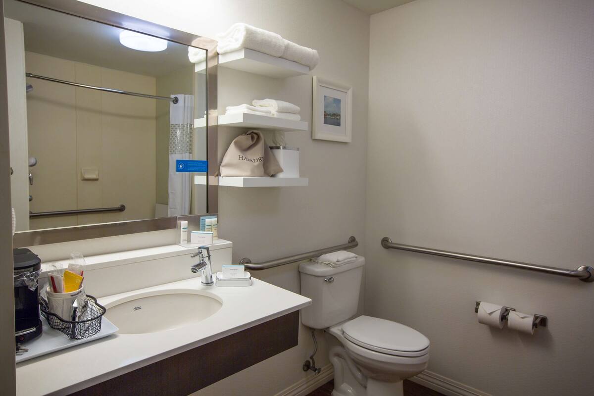 A bathroom with a sink, mirror, towel rack, toilet, and hand dryer.