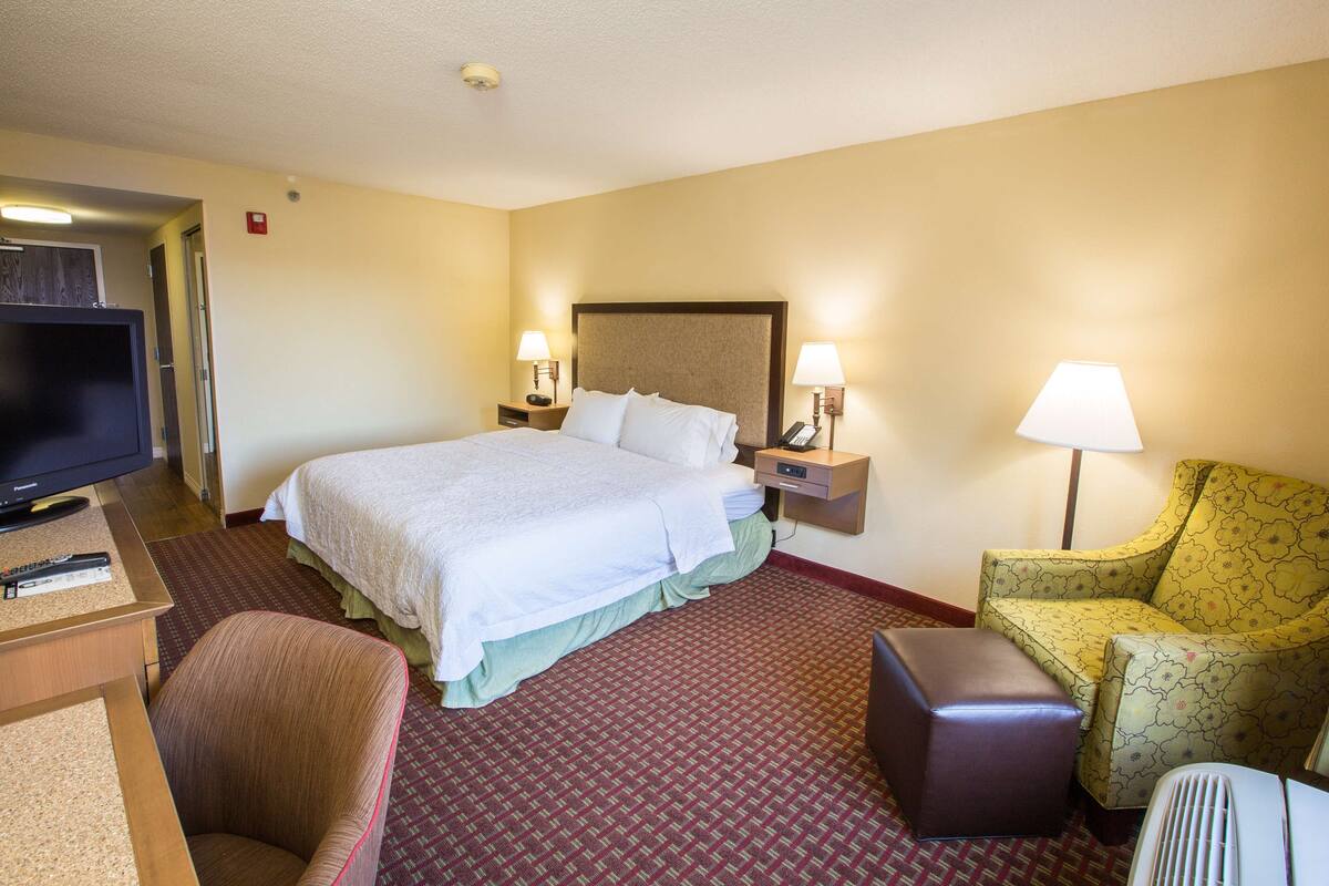 A hotel room with a bed, two bedside lamps, a television, a desk, and a chair.