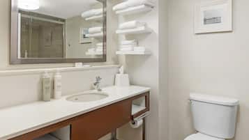 Une salle de bain équipée d’un lavabo, d’un miroir, de porte-serviettes, de toilettes et d’un tableau encadré au mur.