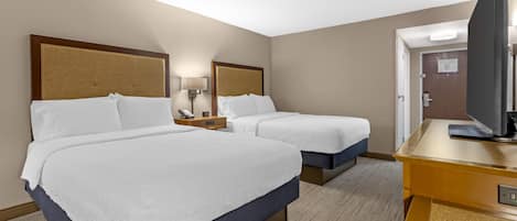 A hotel room with two beds, a desk, a television, and a mirror.