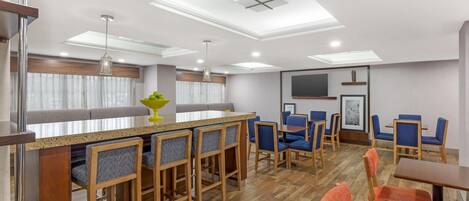 A modern hotel room with a bar area, seating, and a flat-screen TV.