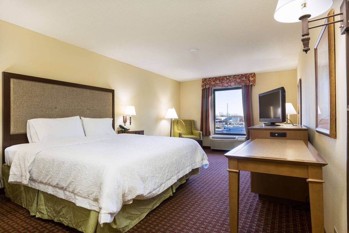 A hotel room with a large bed, a desk, a chair, a television, and a window with a view.