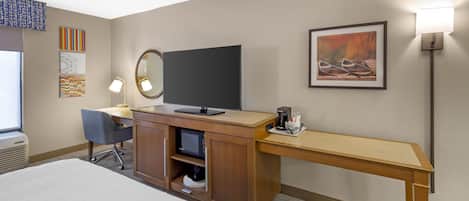 A hotel room with a bed, desk, chair, television, and artwork on the walls.