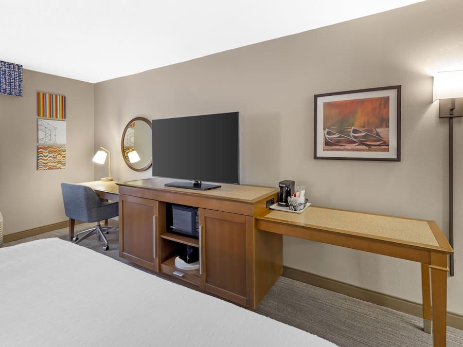 A hotel room with a bed, desk, chair, television, and artwork on the walls.