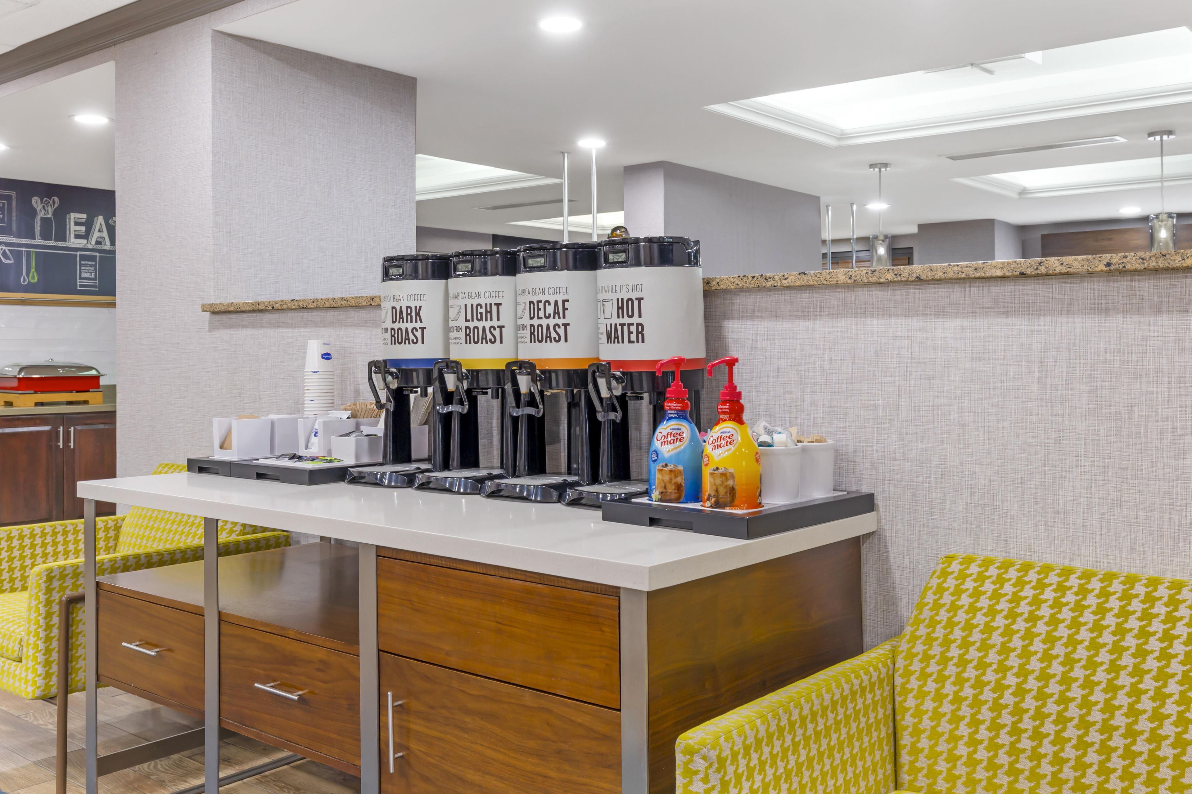 A coffee station with multiple dispensers, a coffee machine, and two bottles of coffee mate.