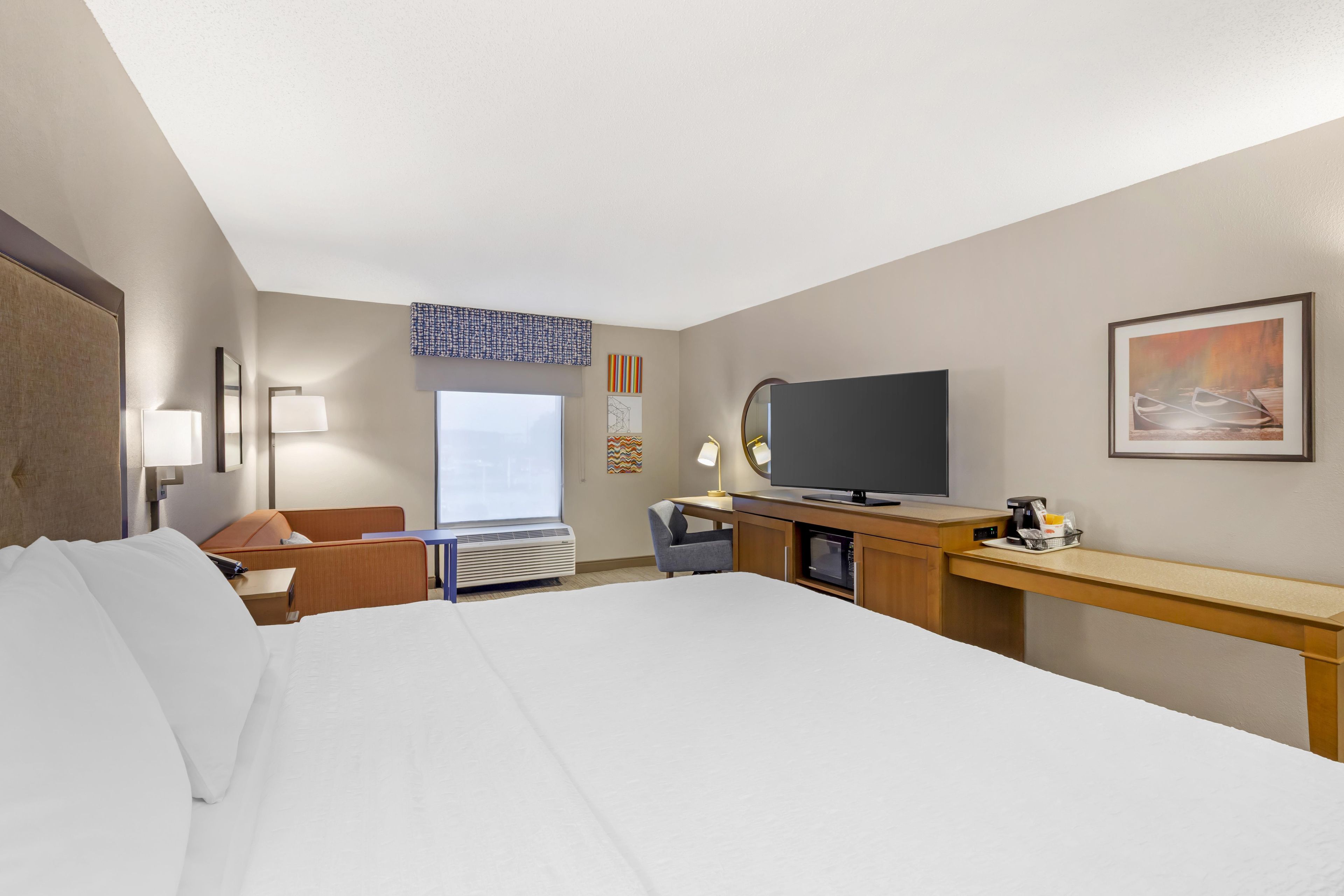 Una habitación de hotel con una cama grande, un escritorio con televisión de pantalla plana, una silla, una lámpara de escritorio y una ventana con vistas.