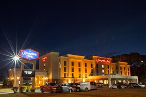A Hampton Inn hotel with a prominent sign, multiple parking spaces, and a well-lit facade.