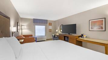 Una camera d'hotel con un letto grande, una scrivania con TV a schermo piatto, una sedia, una lampada da tavolo e una finestra con vista.