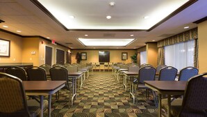 Un salón de conferencias con alfombra estampada, sillas metálicas y mesas dispuestas para reuniones.