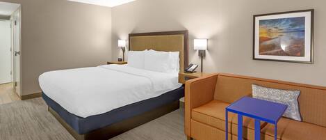 Habitación de hotel con cama, sofá, una mesita, un cuadro en la pared y una puerta.