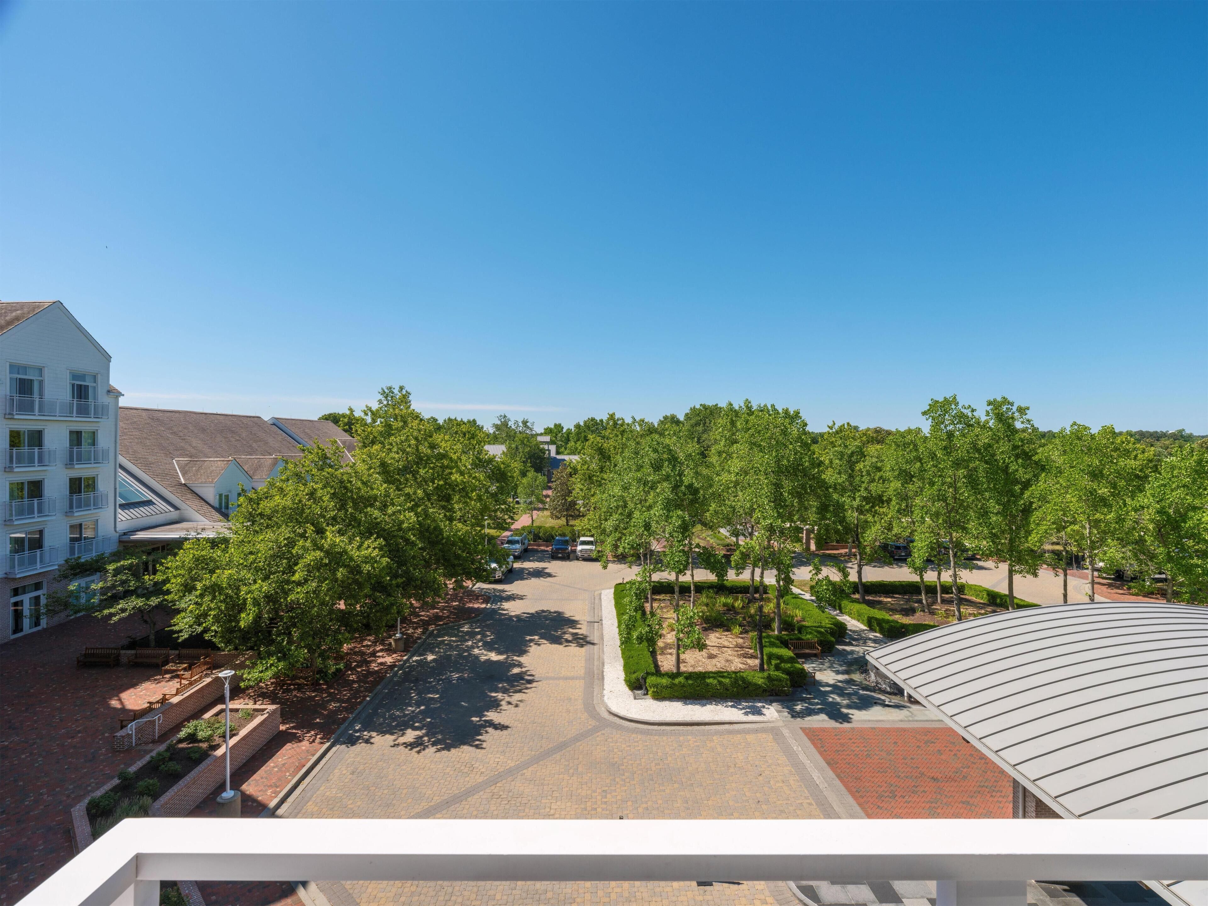A residential area with a paved courtyard, trees, and a multi-story building with balconies.