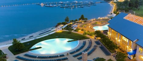 Una località turistica con una grande piscina, posti a sedere all'aperto e vista sul mare.