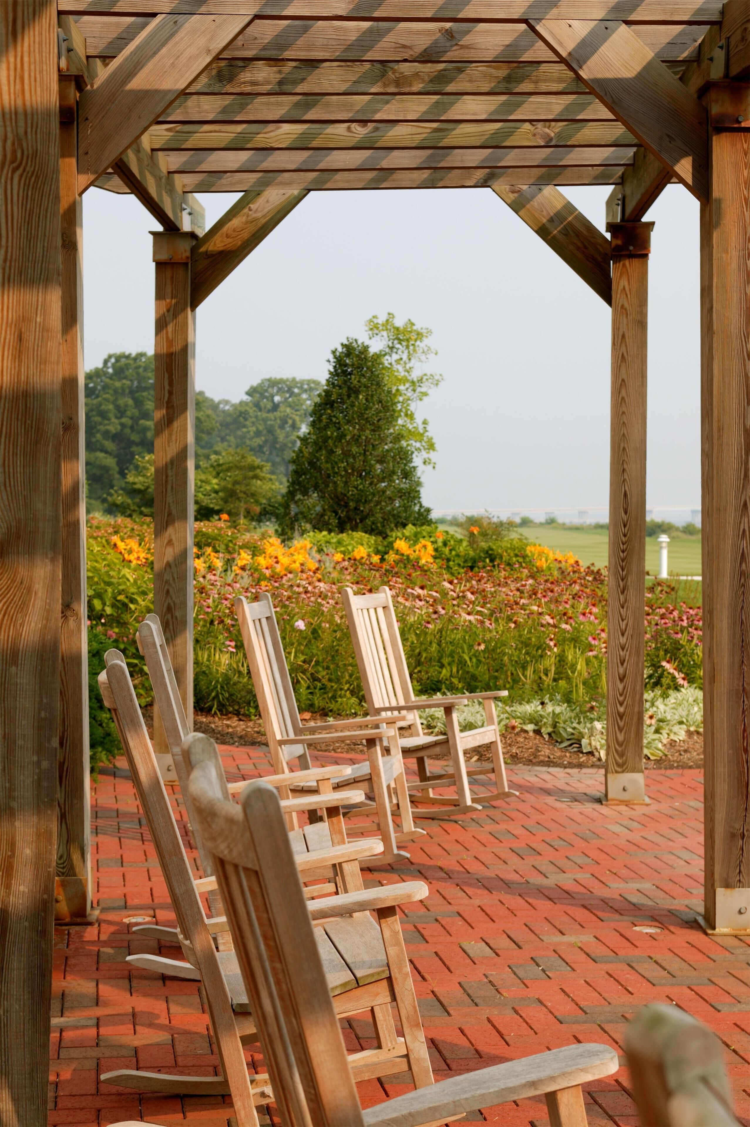 Una pergola in legno con sedie sotto, che si affaccia su un giardino con fiori e alberi.