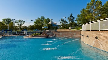 Une piscine bordée d’un mur en briques, dotée d’un poste de surveillance pour les sauveteurs et de chaises longues.