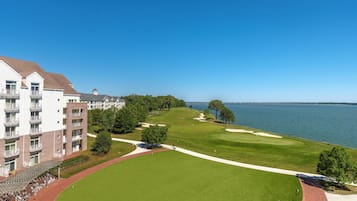 A golf course with a clubhouse, a large body of water, and a bridge in the background.