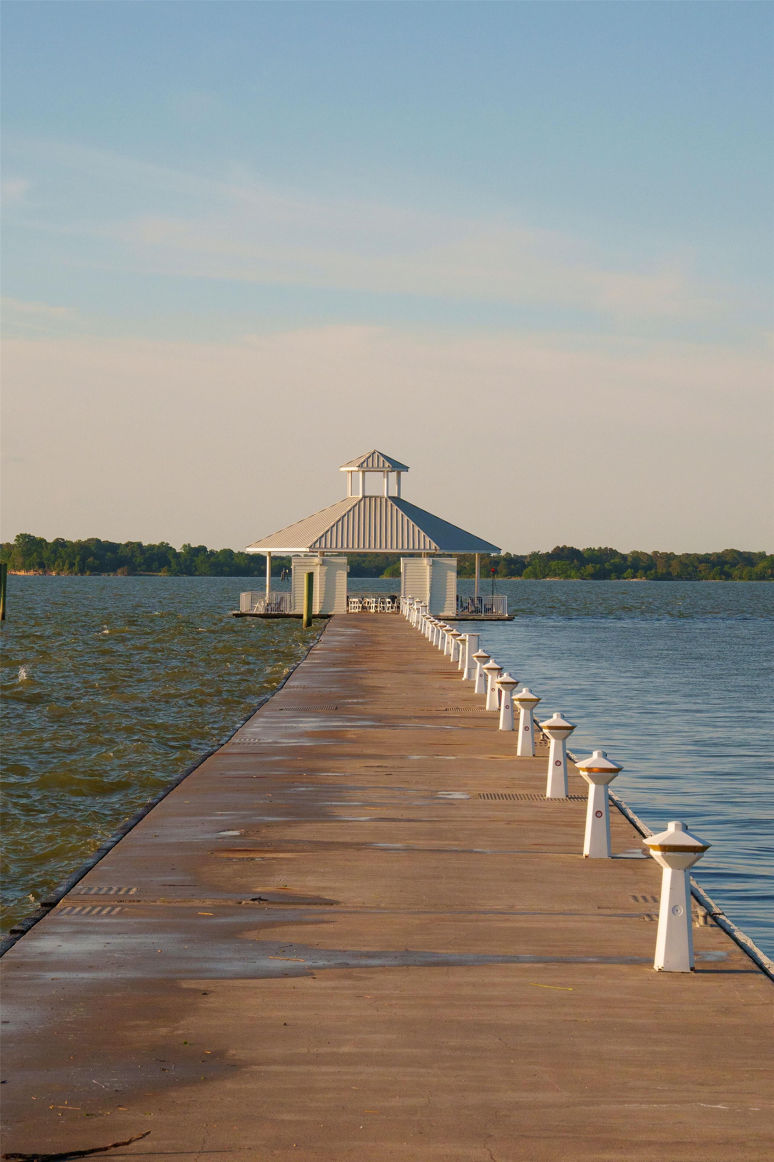 A long concrete pier leading to a white gazebo-like structure with a roof, surrounded by calm water.
