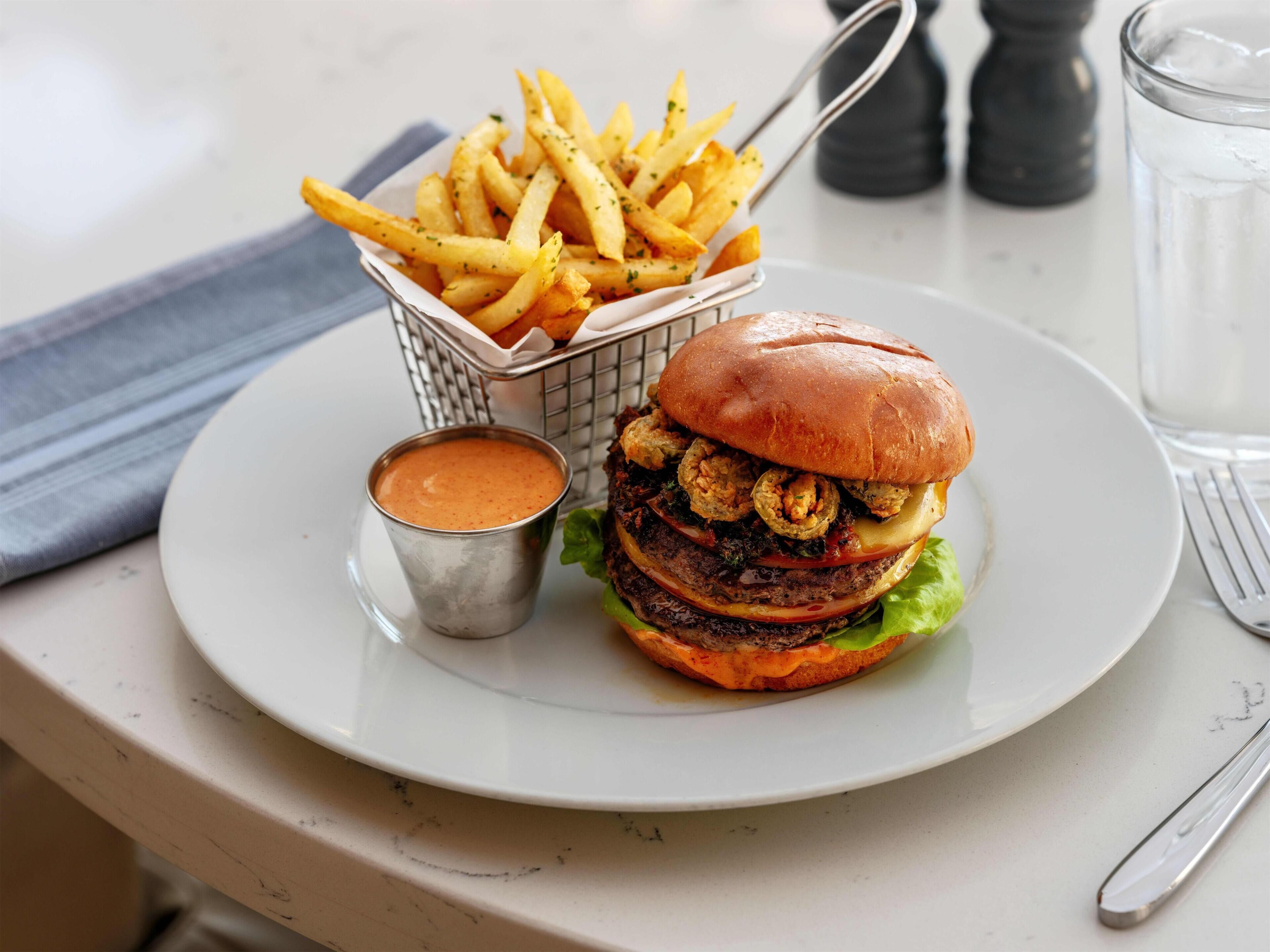 A plate with a burger, fries, and a dipping sauce.