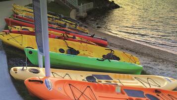 A row of kayaks lined up on a waterfront promenade with a sunset in the background.