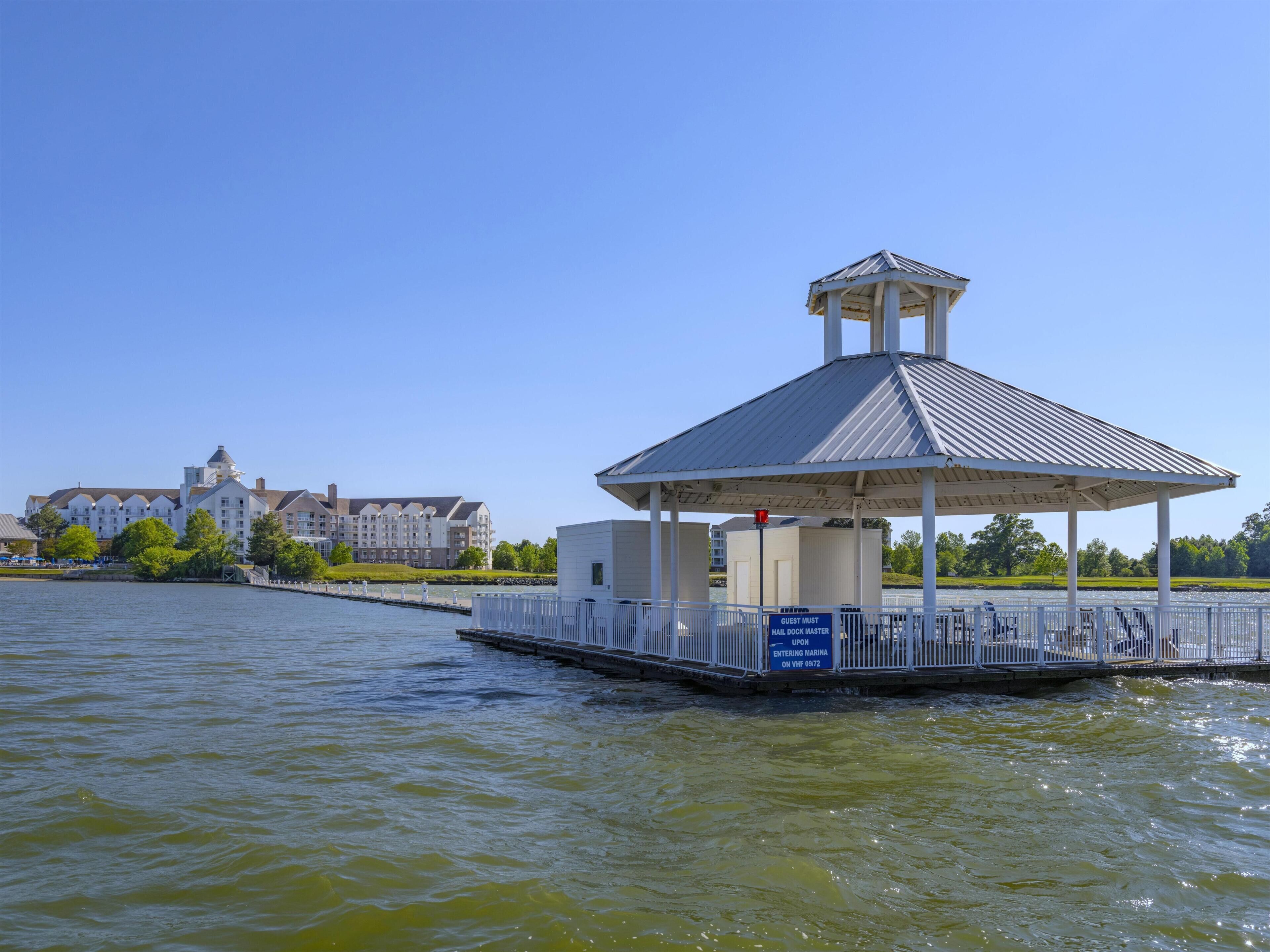 A waterfront gazebo with a metal roof and a white railing, overlooking a body of water.