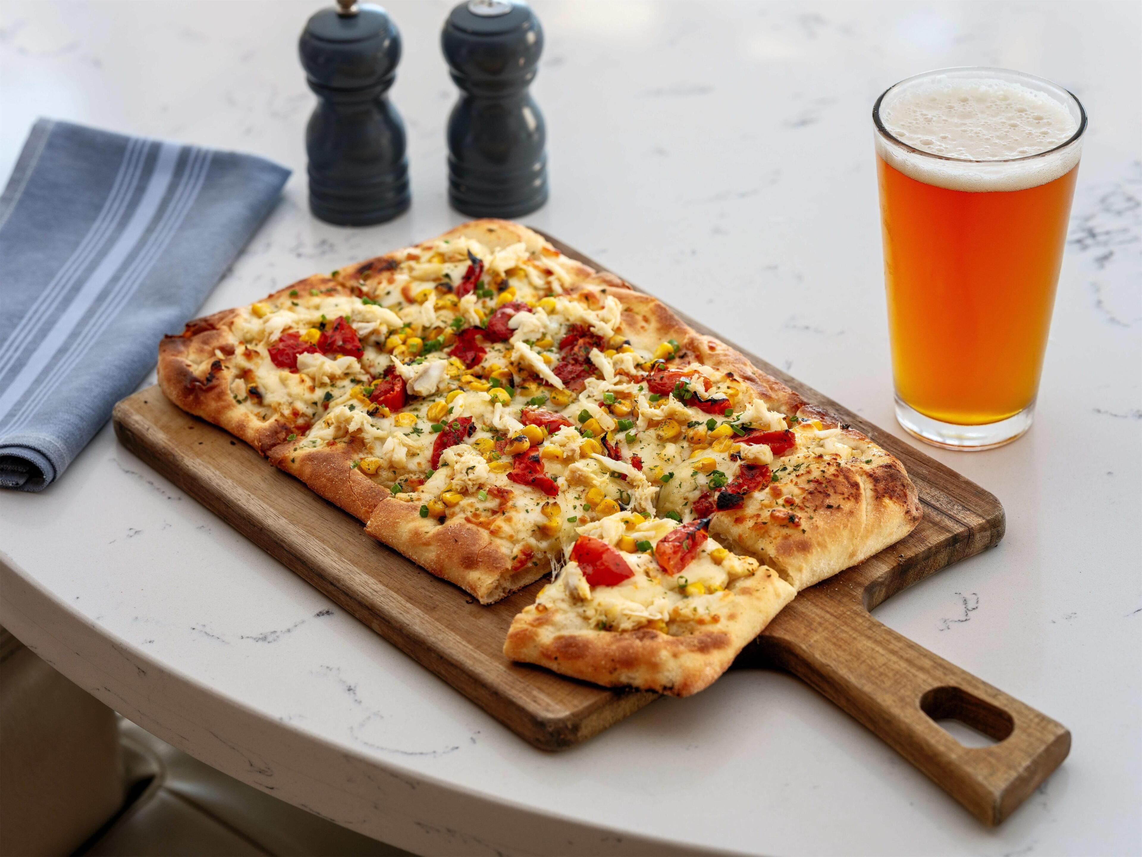 A pizza on a wooden board with a glass of beer beside it.
