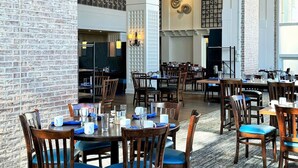 A spacious dining area with multiple tables and chairs, high ceilings with exposed beams, and a brick wall. - Hyatt Regency Chesapeake Bay (Cambridge)