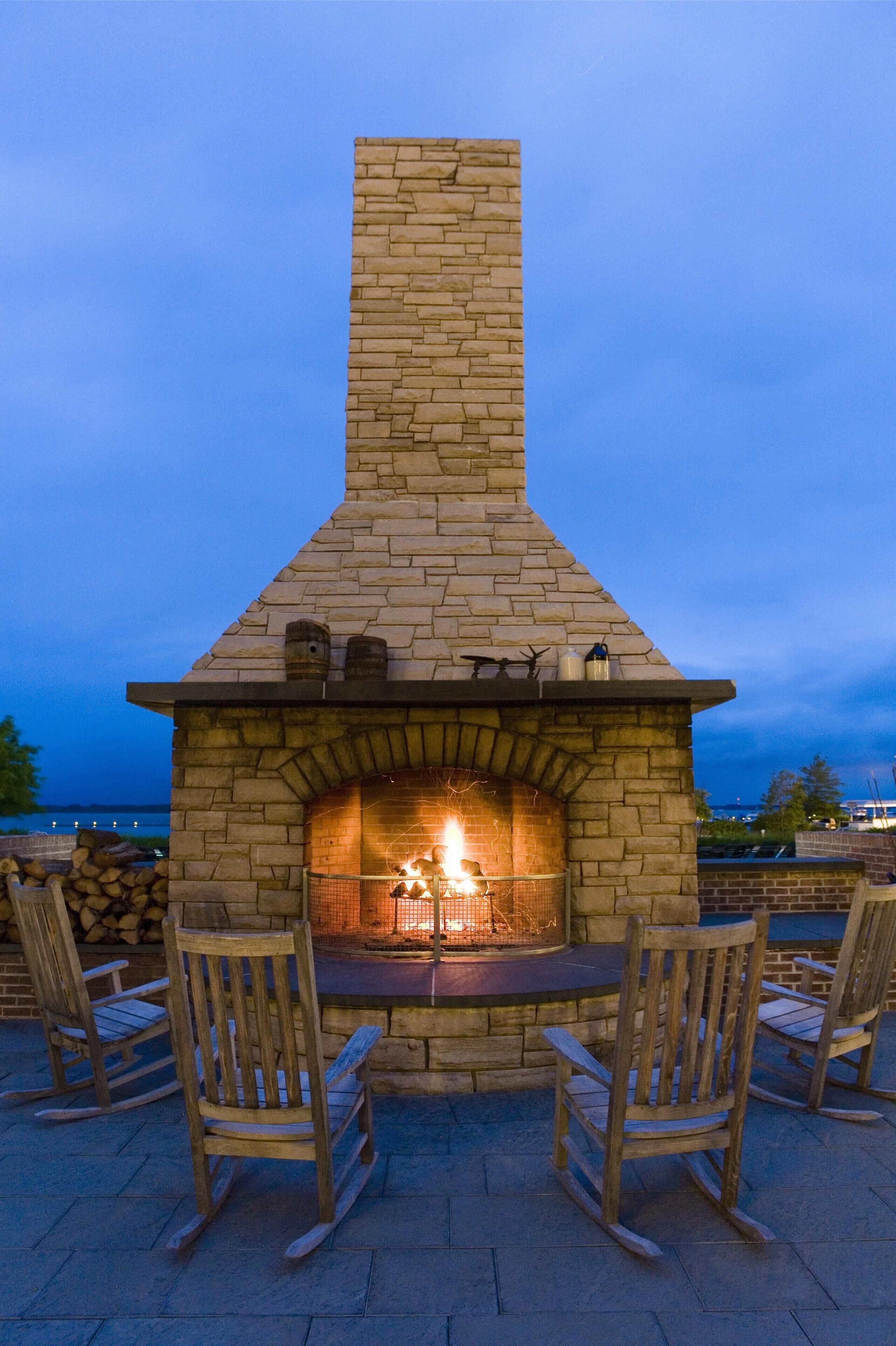 Una chimenea de piedra con chimenea, rodeada de sillas de madera, ubicada en un patio con vista al agua.