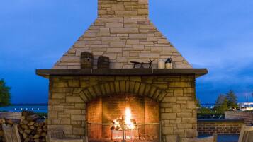 Una chimenea de piedra con chimenea, rodeada de sillas de madera, ubicada en un patio con vista al agua.