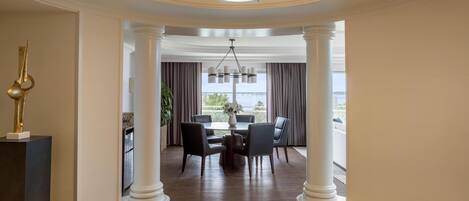 A hotel lobby with a dining area, white columns, a chandelier, and a view of the sea.
