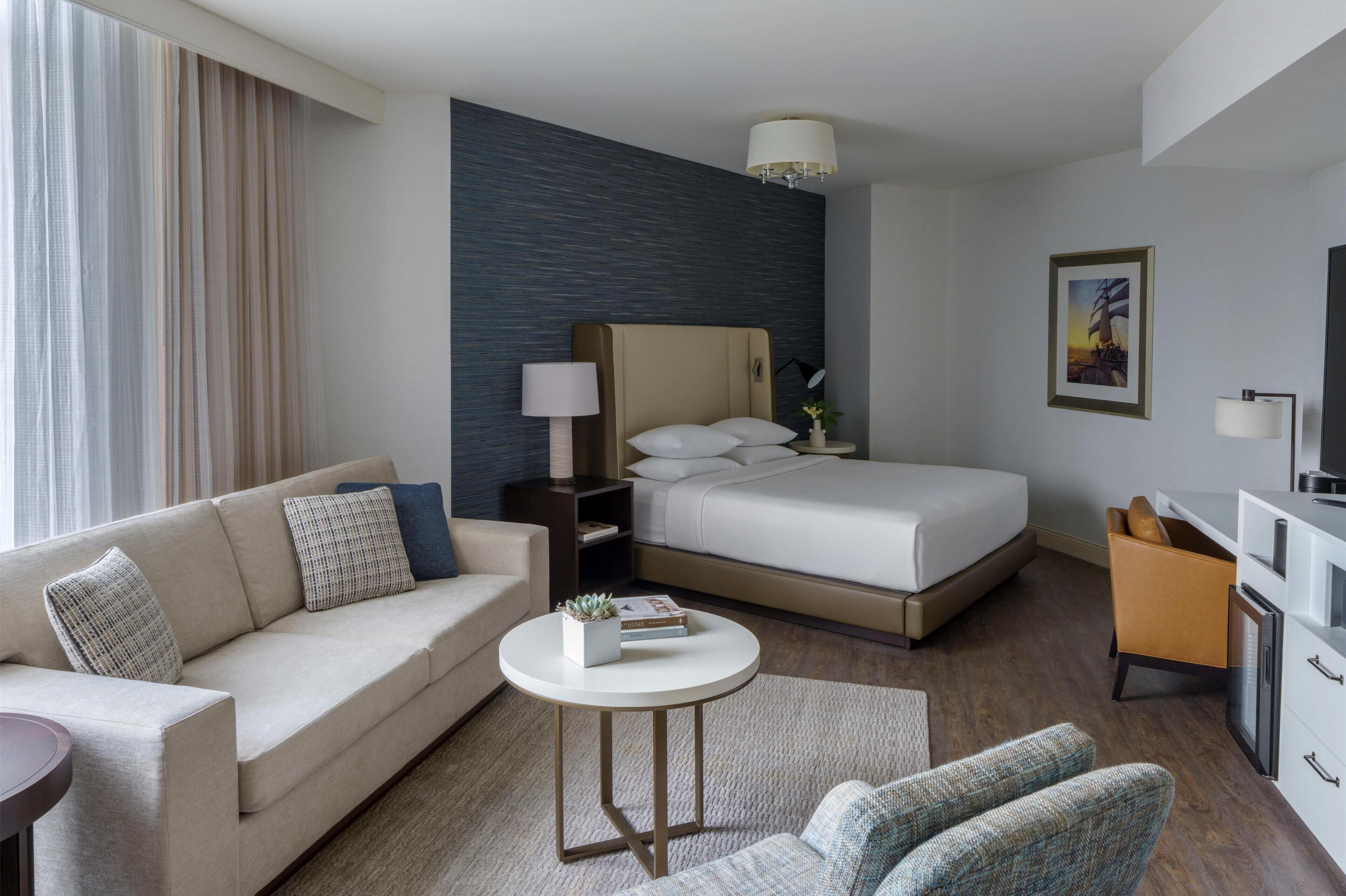 A modern hotel room with a bed, a sofa, a desk, and a small table.