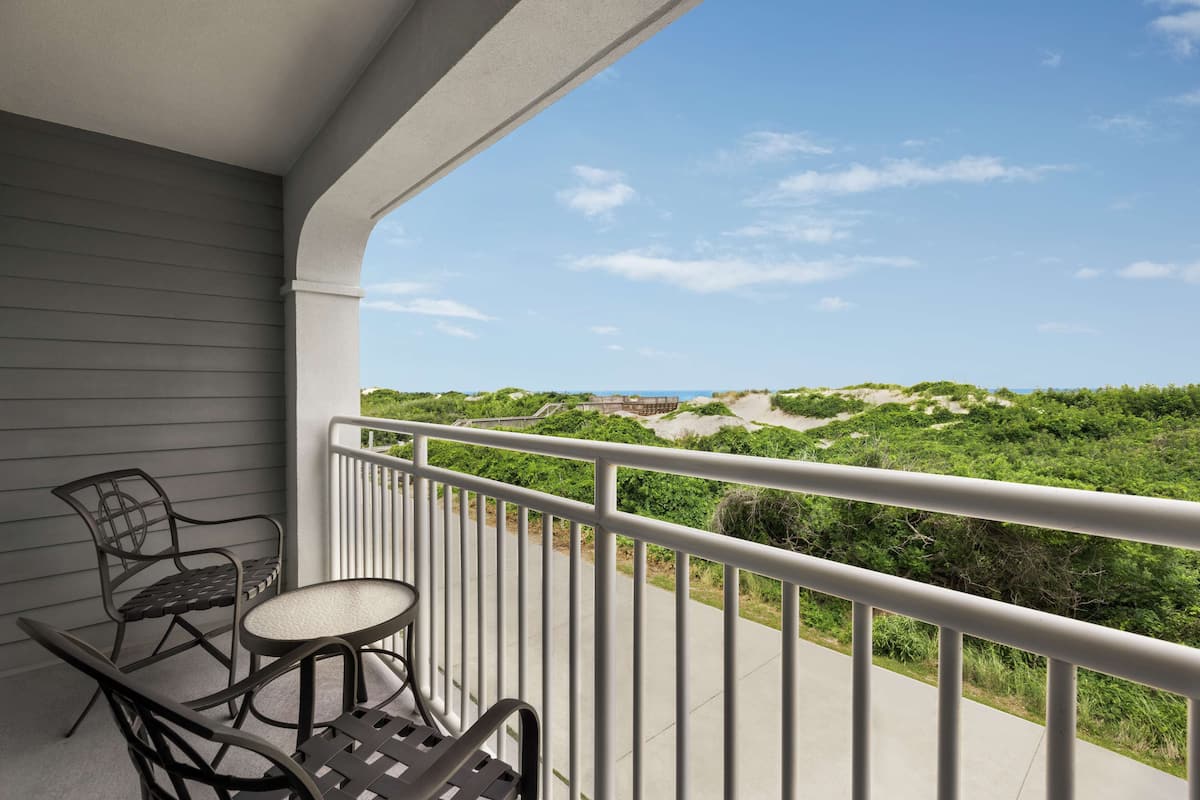 A balcony with a view of a beach and dunes.