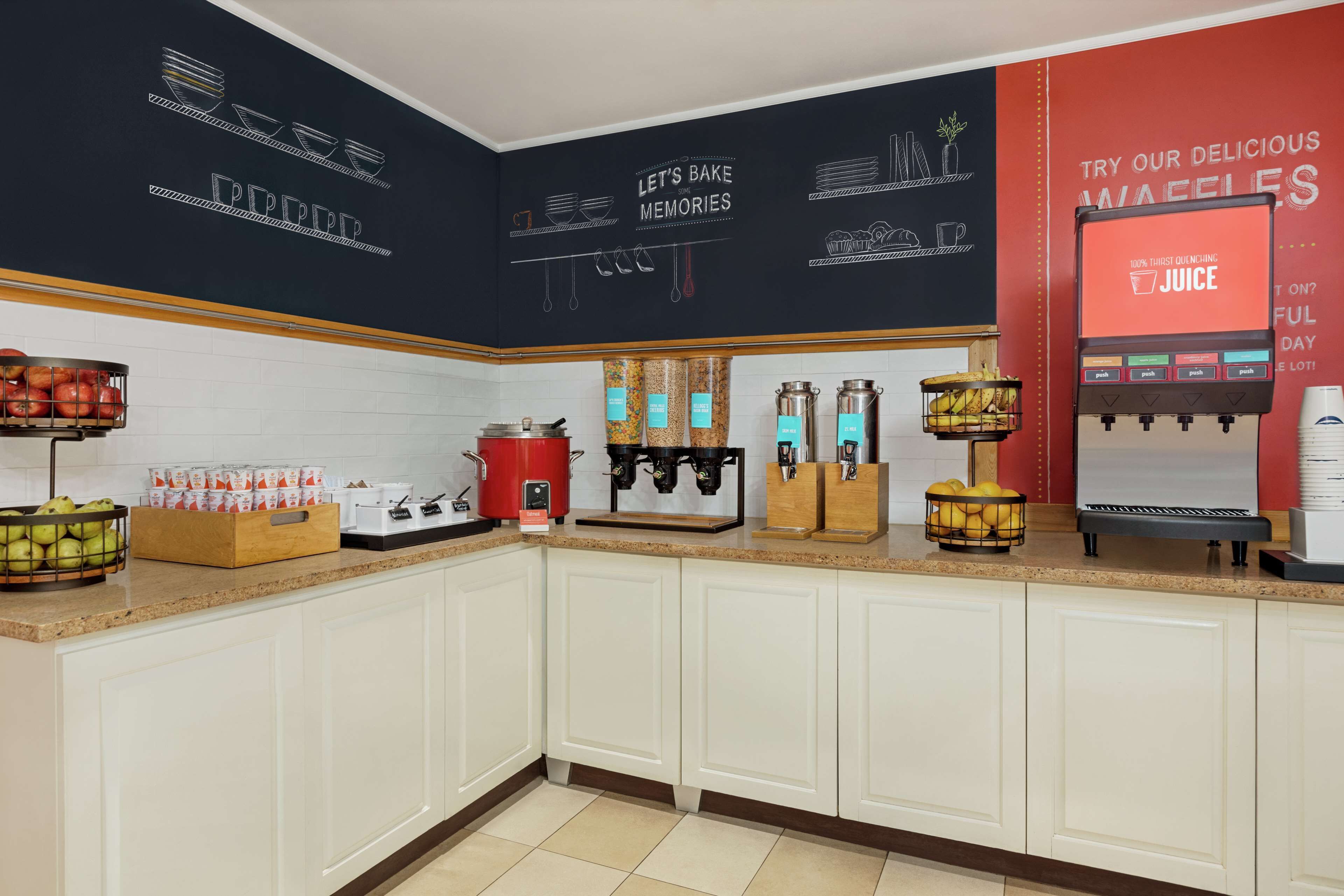 A kitchen area with a coffee machine, fruit baskets, and a juice dispenser.