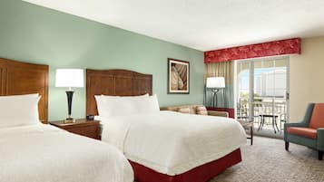A hotel room with two beds, a sitting area with a chair, a balcony with a view, and a ceiling fan.
