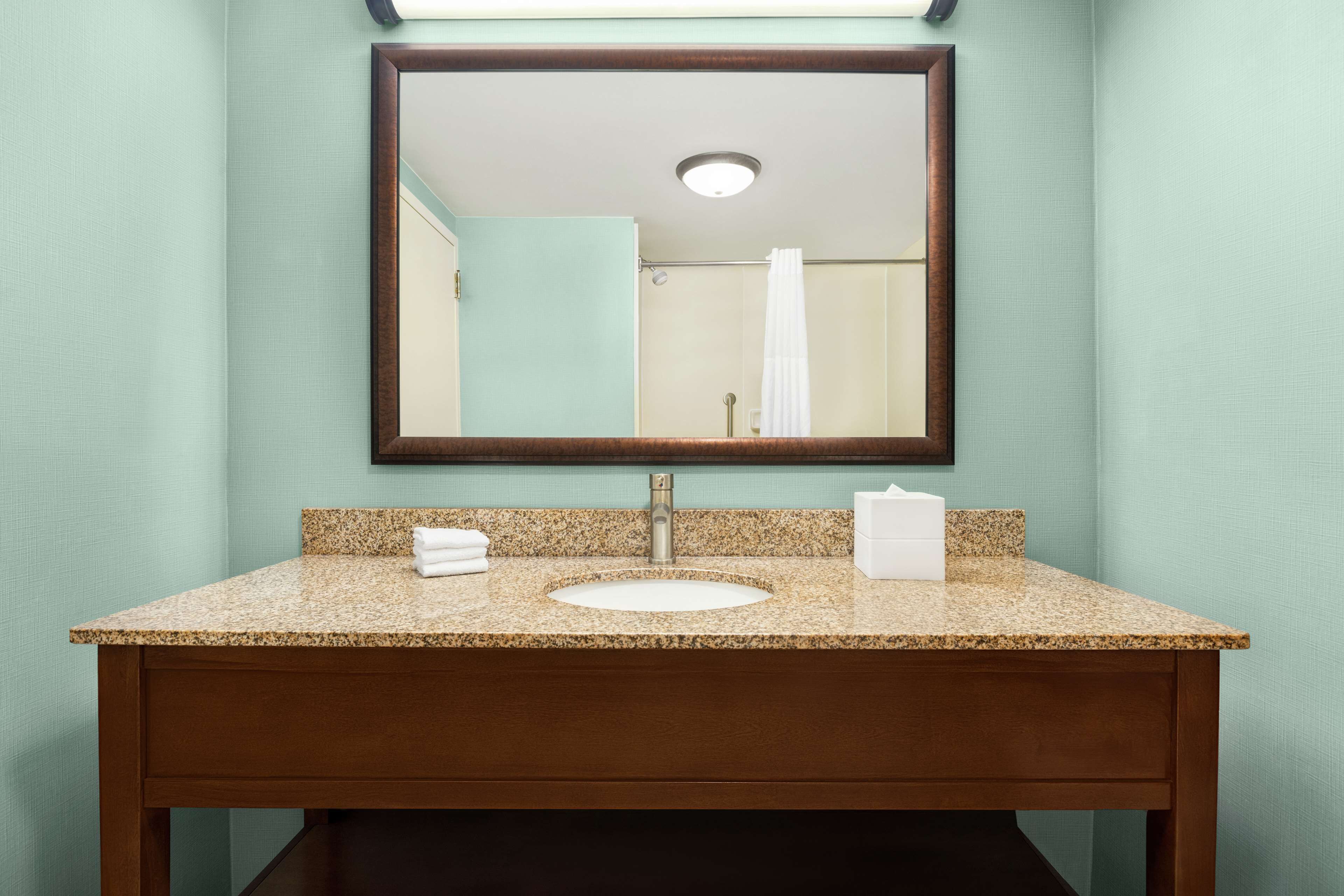 A bathroom with a granite countertop sink, a mirror, and a towel rack.