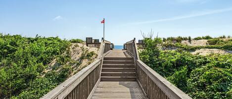A wooden boardwalk leading to a beach with a flag at the end.