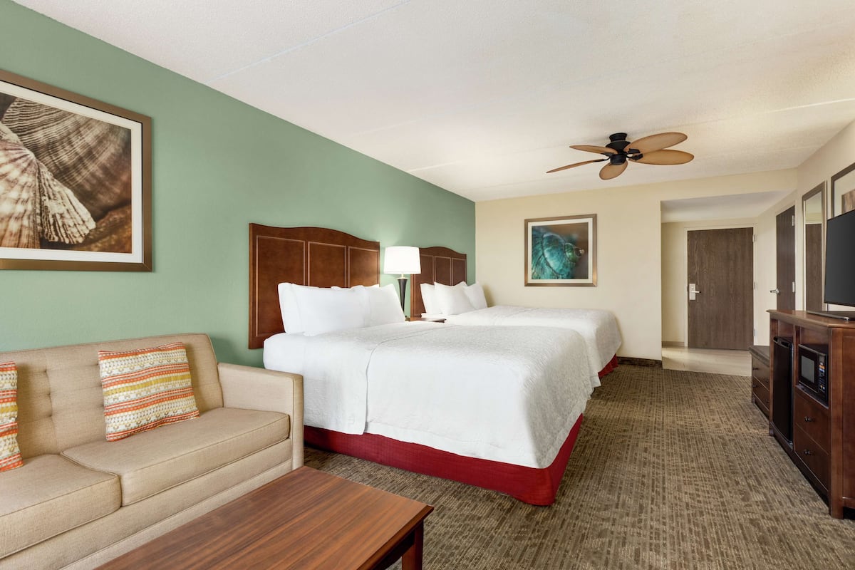 A hotel room with a bed, a sofa, a TV, and a ceiling fan.