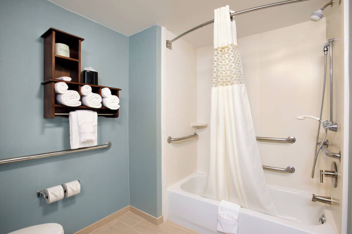 A bathroom with a bathtub, a shower, a toilet, and a shelf with towels.