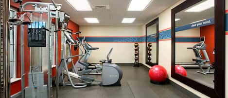 A gym with exercise equipment, a mirror, and a motivational quote on the wall.