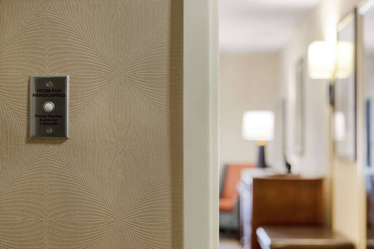 A wall with a sign indicating a room for handicapped individuals and a button to press for 5 seconds.