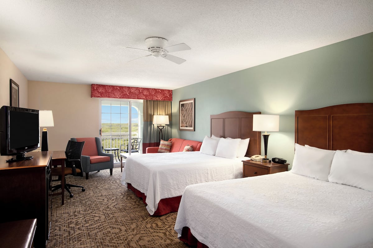 A hotel room with two beds, a desk with a TV, a chair, a desk lamp, and a window with a view.