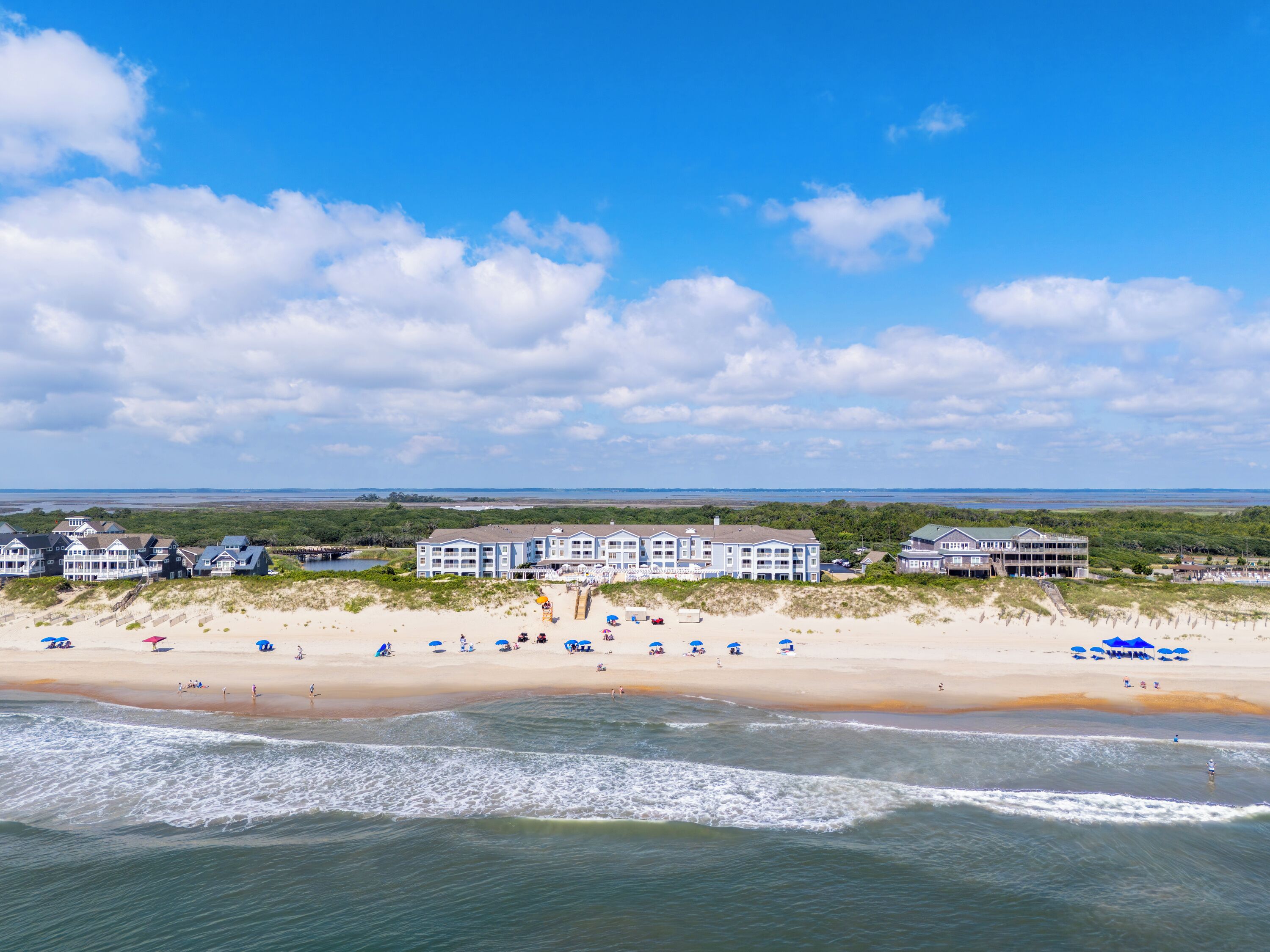 A beachfront hotel with multiple buildings, a sandy beach, and ocean waves.