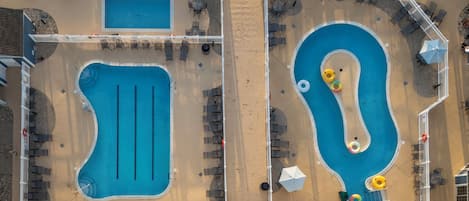 Vista aérea de una zona de piscina con dos piscinas separadas, tumbonas, sombrillas y una valla blanca.