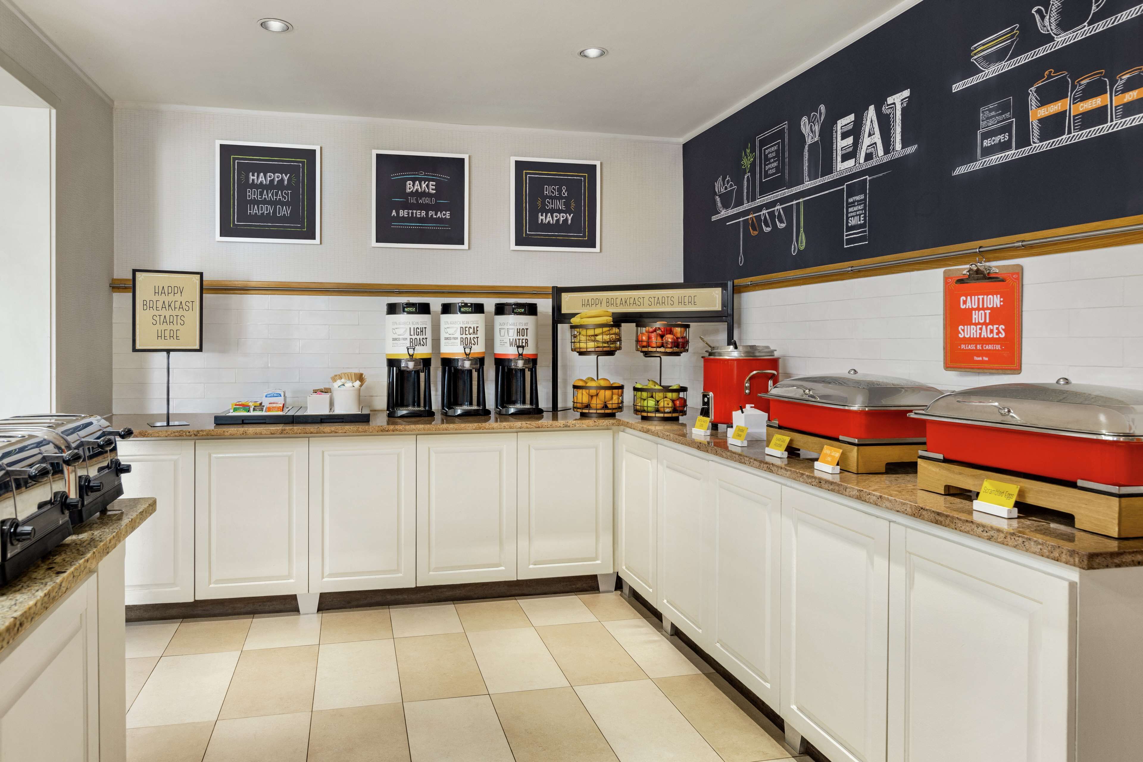 A breakfast bar with coffee makers, a fruit display, and a caution sign for hot surfaces.