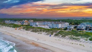 Un hotel frente a la playa con varias edificaciones, una playa de arena y olas oceánicas.