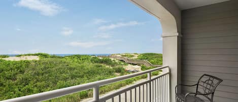 A balcony with a view of a beach and dunes, featuring a metal railing and two chairs.